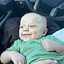 baby, child, smiling, green_shirt, car_interior, person, hand, face, happy, infant, closeup, portrait, sitting, holding, cute, skin, head, eyes, clothing, seat