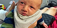 Baylor joined the competition — help win amazing prizes! baby, infant, hand, striped_bib, striped_clothing, indoor, bed, door, blanket, person, young_child, skin, face, expression, holding, comfort, room, casual, furniture, home