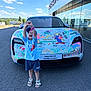 child, car, porsche, colorful, drawing, hood, road, building, glass, reflection, sky, clouds, happy, smiling, shorts, sandals, cap, outdoor, daylight, asphalt