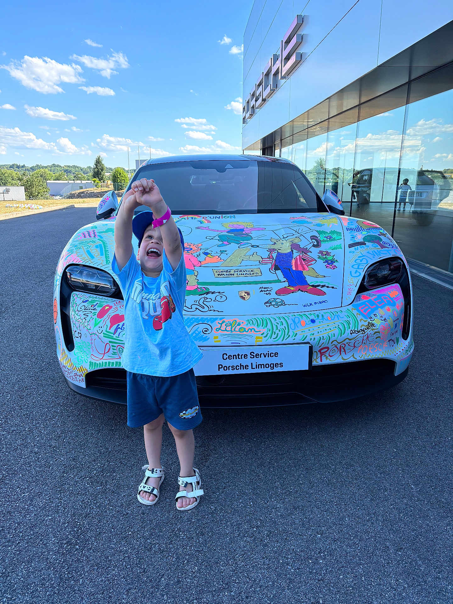 Thyam participe au concours pour gagner de l'argent avec cette photo : child, car, porsche, colorful, drawing, hood, road, building, glass, reflection, sky, clouds, happy, smiling, shorts, sandals, cap, outdoor, daylight, asphalt