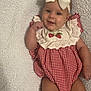 baby, infant, smiling, headband, bow, red_and_white, gingham, dress, strawberry, embroidered, white_blanket, soft_texture, cute, happy, fist, lying_down, sock, footwear, indoors, portrait