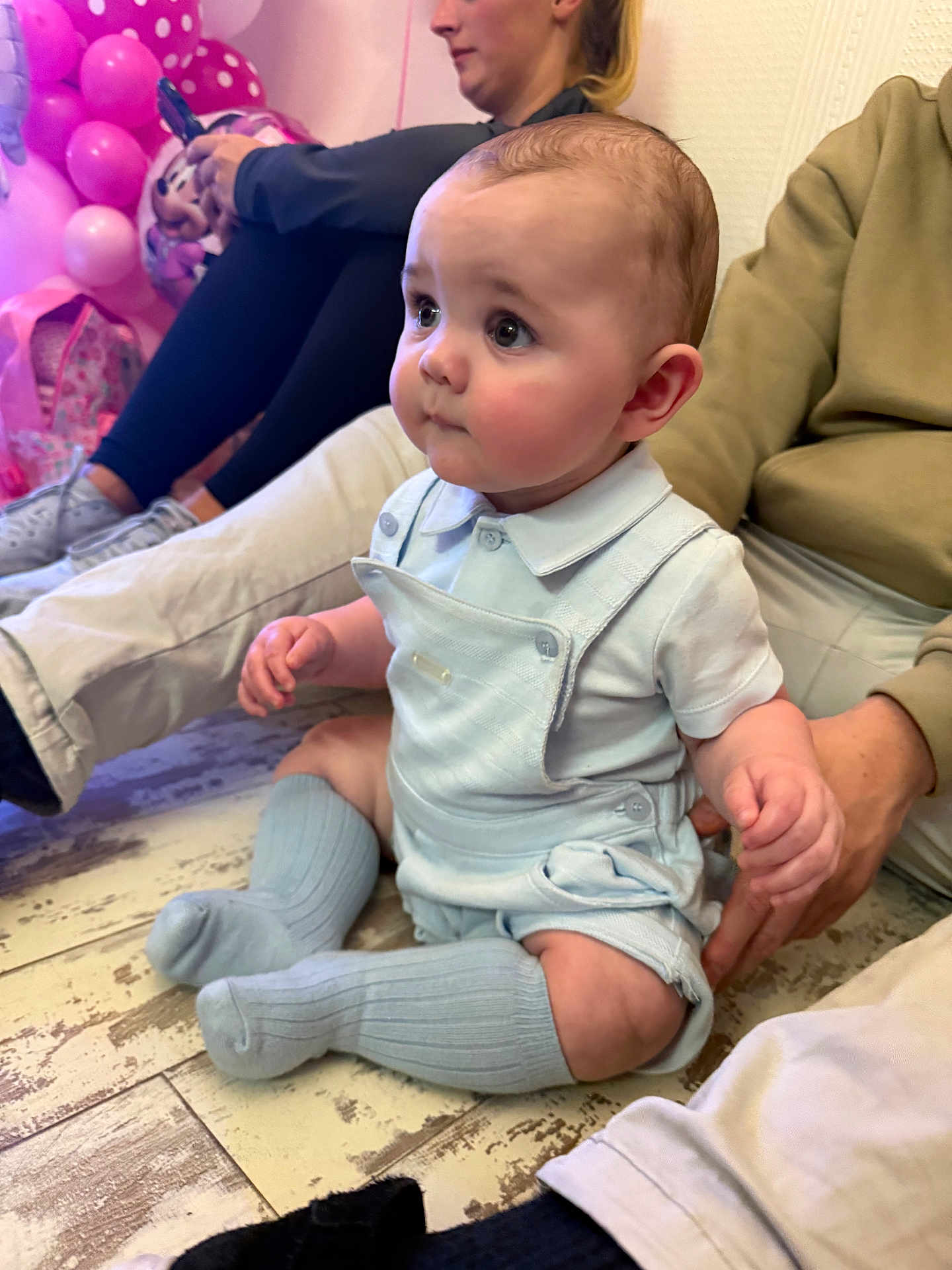 Shae is registered to the contest to win money with this photo: baby, child, infant, floor, socks, overalls, person, adult, balloons, pink, party, seated, wood_floor, clothing, cute, indoor, people, hand, face, portrait