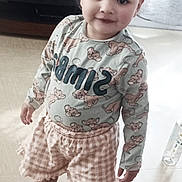 Mia participe au concours pour gagner de l'argent avec cette photo : child, smiling, indoor, person, clothing, hair_buns, shorts, long_sleeve_shirt, floor, couch, bottle, cute, standing, young_child, portrait, playful, happy, home, furniture, light
