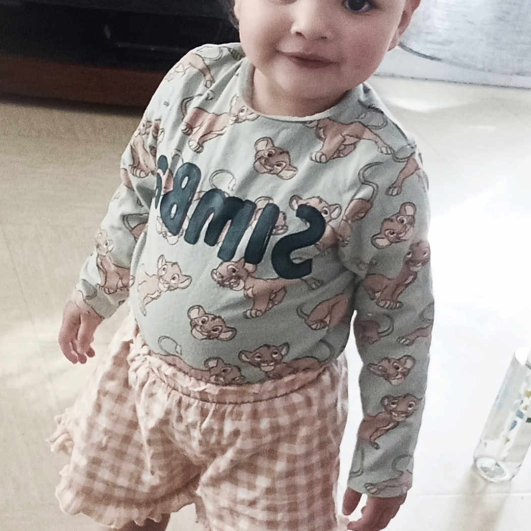 Mia participe au concours pour gagner de l'argent avec cette photo : bottle, child, clothing, couch, cute, floor, furniture, hair_buns, happy, home, indoor, light, long_sleeve_shirt, person, playful, portrait, shorts, smiling, standing, young_child