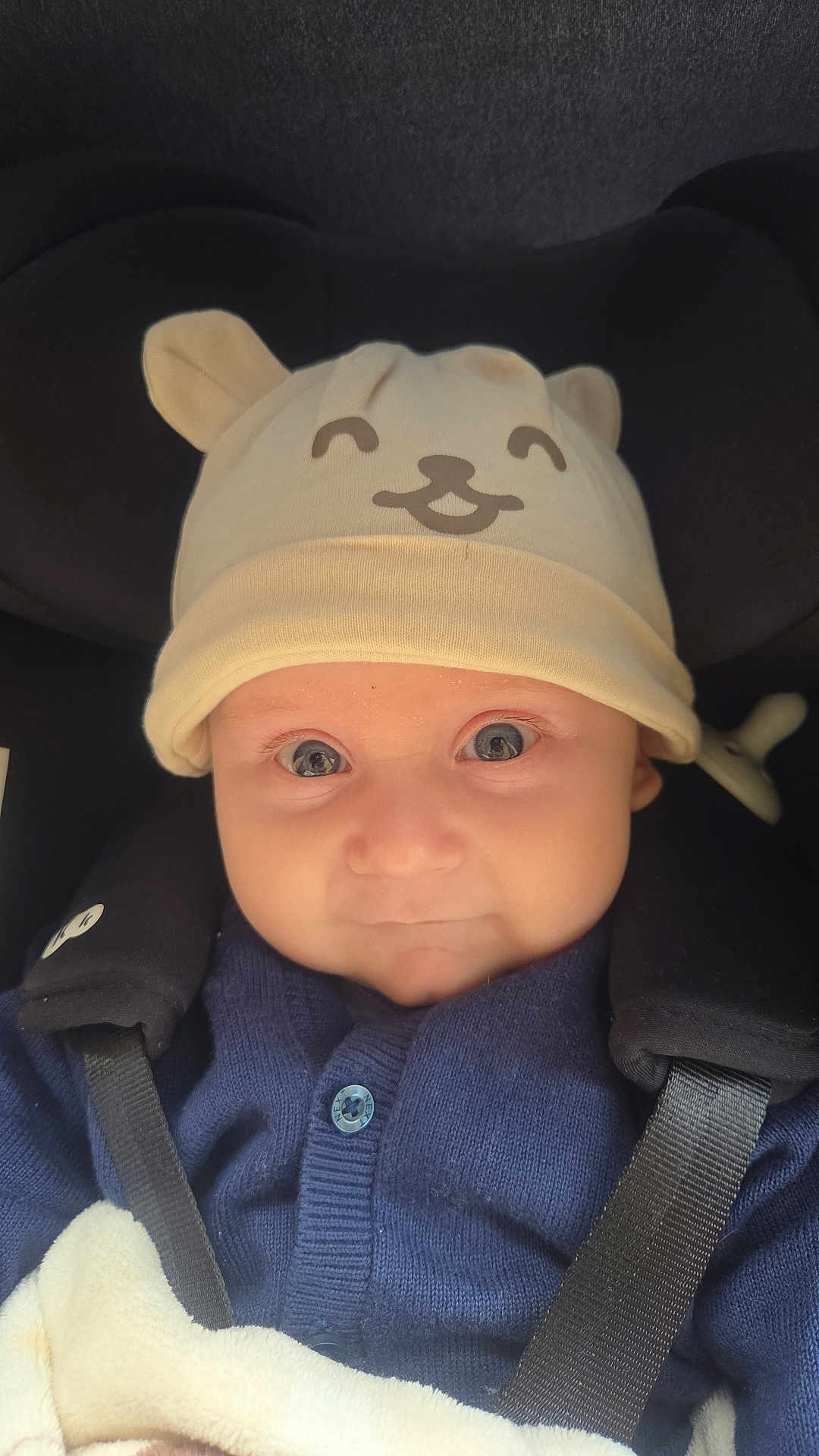 Noah joined the competition — help win amazing prizes! baby, child, hat, bear_ears, car_seat, seatbelt, blue_sweater, blanket, face, eyes, cute, infant, smile, clothing, portrait, indoors, closeup, baby_accessory, warm, child_seat