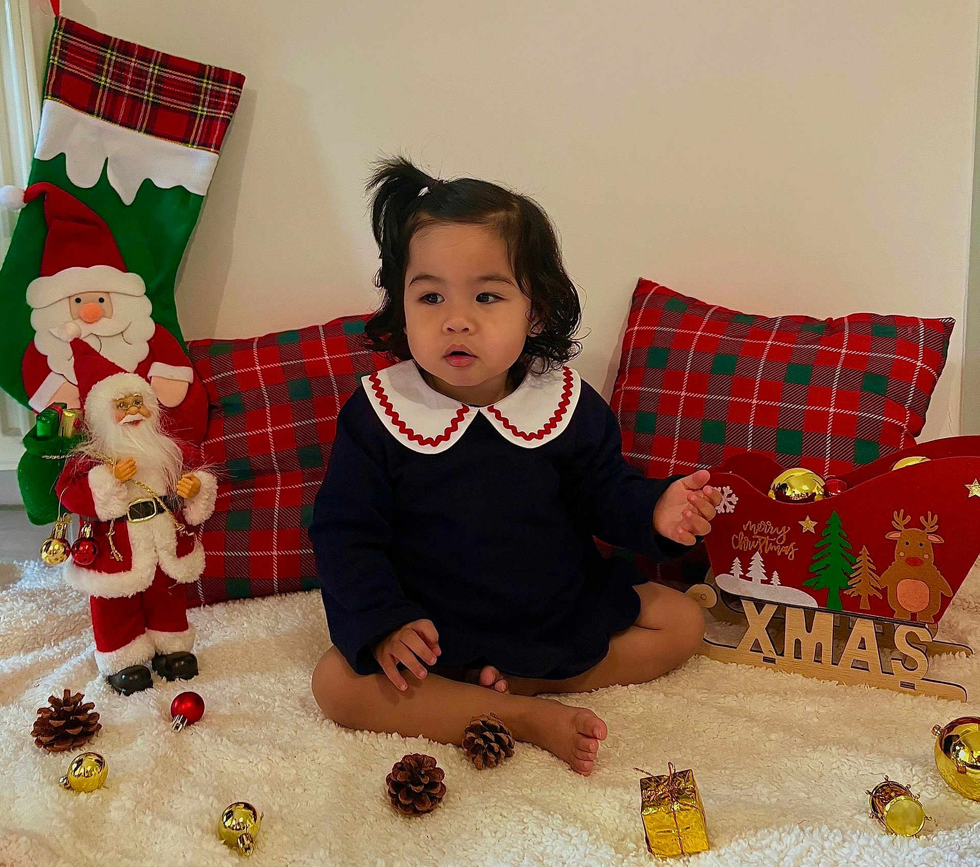 Kelyana participe au concours pour gagner de l'argent avec cette photo : toddler, child, holiday, christmas, santa_claus, plaid, pillow, decorations, pinecones, baubles, toy, sleigh, xmas, indoor, carpet, cute, curly_hair, navy_dress, white_collar, festive