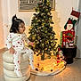 Kelyana participe au concours pour gagner de l'argent avec cette photo : toddler, child, christmas_tree, holiday_decor, pajamas, heart_pattern, ornaments, lights, santa_figurine, stocking, cushion, floor, indoor, plush, toy, festive, decorations, warm_lighting, seated, curly_hair