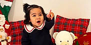 Kelyana a rejoint le concours — aidez-le/la à gagner de superbes lots ! toddler, child, smiling, pointing, sitting, indoor, plush_toy, teddy_bear, christmas_decorations, santa_figurine, pillow, plaid_pattern, pine_cone, ornament, holiday, white_rug, black_clothing, cute, happy, portrait