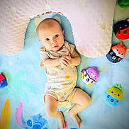 Luna joined the competition — help win amazing prizes! baby, infant, child, portrait, lying_down, indoors, blanket, pillow, plush_toys, stuffed_animals, colorful, smiling, wide_eyes, romper, nursery, playmat, numbers, soft_furnishings, overhead_view, photography