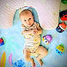 baby, infant, child, portrait, lying_down, indoors, blanket, pillow, plush_toys, stuffed_animals, colorful, smiling, wide_eyes, romper, nursery, playmat, numbers, soft_furnishings, overhead_view, photography