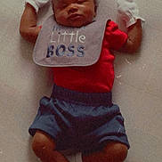 Skylan is registered to the contest to win money with this photo: baby, sleeping, infant, clothing, bib, red_shirt, blue_shorts, white_socks, mittens, lying_down, cute, peaceful, indoor, portrait, child, newborn, soft_surface, small_person, resting, adorable