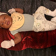 Skylan is registered to the contest to win money with this photo: baby, blanket, comfort, cozy, cute, expression, face, hat, indoors, infant, lying_down, mittens, pajamas, patterned_clothing, person, portrait, sleepwear, soft_toys, warm_colors, young_child