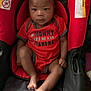 baby, black, car_seat, child, clothing, cute, expression, face, foot, hand, indoors, infant, onesie, person, portrait, red, seat, sitting, warning_label, young_child