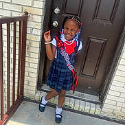 Logan joined the competition — help win amazing prizes! child, girl, smiling, dress, plaid, sash, grad, door, beads, hair, bracelet, white_shirt, black_shoes, socks, outdoor, concrete, railing, brick_wall, happy, portrait