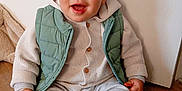 Lyzio participe au concours pour gagner de l'argent avec cette photo : baby, toddler, child, smiling, sitting, indoor, wooden_floor, green_vest, knit_sweater, buttons, striped_socks, pants, face, eyes, hands, legs, portrait, white_wall, cute, happy