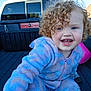 child, toddler, curly_hair, blue_eyes, onesie, pastel_colors, smiling, outdoor, pickup_truck, vehicle, playful, happy, face, person, daylight, clothing, baby, reaching, cute, fun