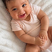 Atalia joined the competition — help win amazing prizes! baby, blanket, child, cozy, curly_hair, cute, cute_expression, face, happy, human, indoors, infant, lying_down, onesie, portrait, relaxed, skin, small_hands, smiling, soft_texture