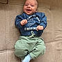 baby, infant, smiling, blue_sweatshirt, green_pants, sock, couch, furniture, happy, face, person, child, clothing, indoors, cute, playful, young, sitting, cozy, portrait