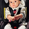 Neda is registered to the contest to win money with this photo: baby, child, car_seat, infant, portrait, sitting, indoors, harness, seatbelt, pacifier, white_clothing, hoodie, blond_hair, blue_eyes, hands, smiling, vehicle, safety_seat, close_up, photography