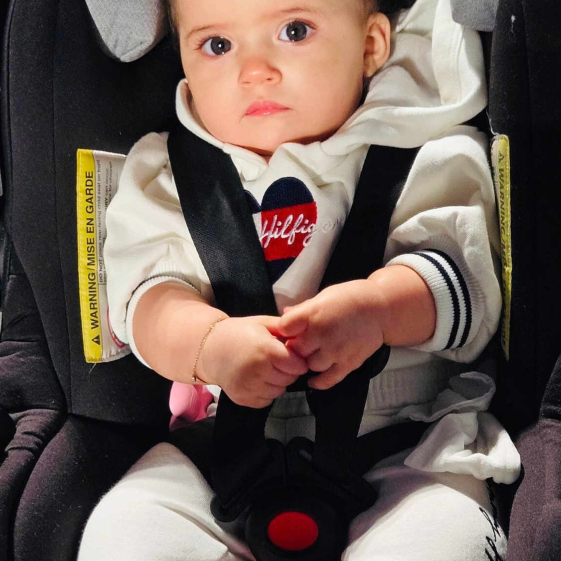 Neda is registered to the contest to win money with this photo: baby, child, car_seat, infant, portrait, sitting, indoors, harness, seatbelt, pacifier, white_clothing, hoodie, blond_hair, blue_eyes, hands, smiling, vehicle, safety_seat, close_up, photography