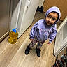 Isabella is registered to the contest to win money with this photo: child, hoodie, purple_clothing, butterfly_pattern, pants, black_shoes, wooden_floor, kitchen, yellow_container, curious_expression, standing, indoors, door, cabinet, flooring, appliance, person, small_child, casual_clothing, looking_up