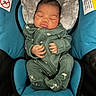 newborn, baby, sleeping, car_seat, green_onesie, infant, headrest, cushion, warning_label, child, peaceful, cute, small_hands, soft_fabric, indoor, portrait, resting, cozy, child_safety, blue_cushion