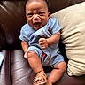 Ace is registered to the contest to win money with this photo: baby, infant, child, blue_clothing, romper, sandals, leather_couch, pillow, fist, smiling, happy, cute, indoors, portrait, sitting, skin, face, hand, foot, expression