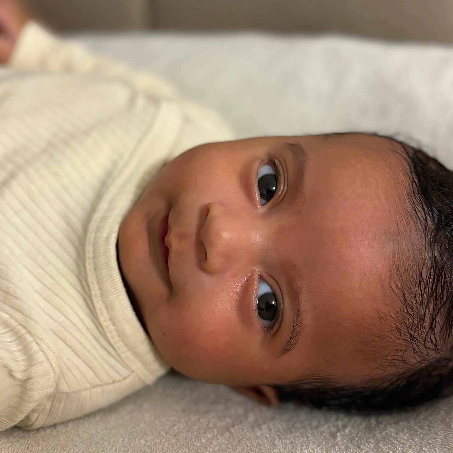 Nohé participe au concours pour gagner de l'argent avec cette photo : baby, child, close_up, clothing, cozy, cream, cute, expression, eyes, face, head, indoors, infant, lying_down, person, portrait, ribbed, skin, soft_surface, young