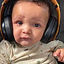 baby, infant, child, headphones, headset, portrait, closeup, onesie, clothing, curly_hair, big_eyes, facial_expression, face, sitting, couch, indoor, audio_device, toddler, cute, hand