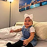 Hanna joined the competition — help win amazing prizes! baby, child, smiling, sitting, bedroom, bed, bedding, pillow, bow, headband, denim, overalls, black_socks, portrait, indoors, lamp, wall_art, cityscape, happy, infant
