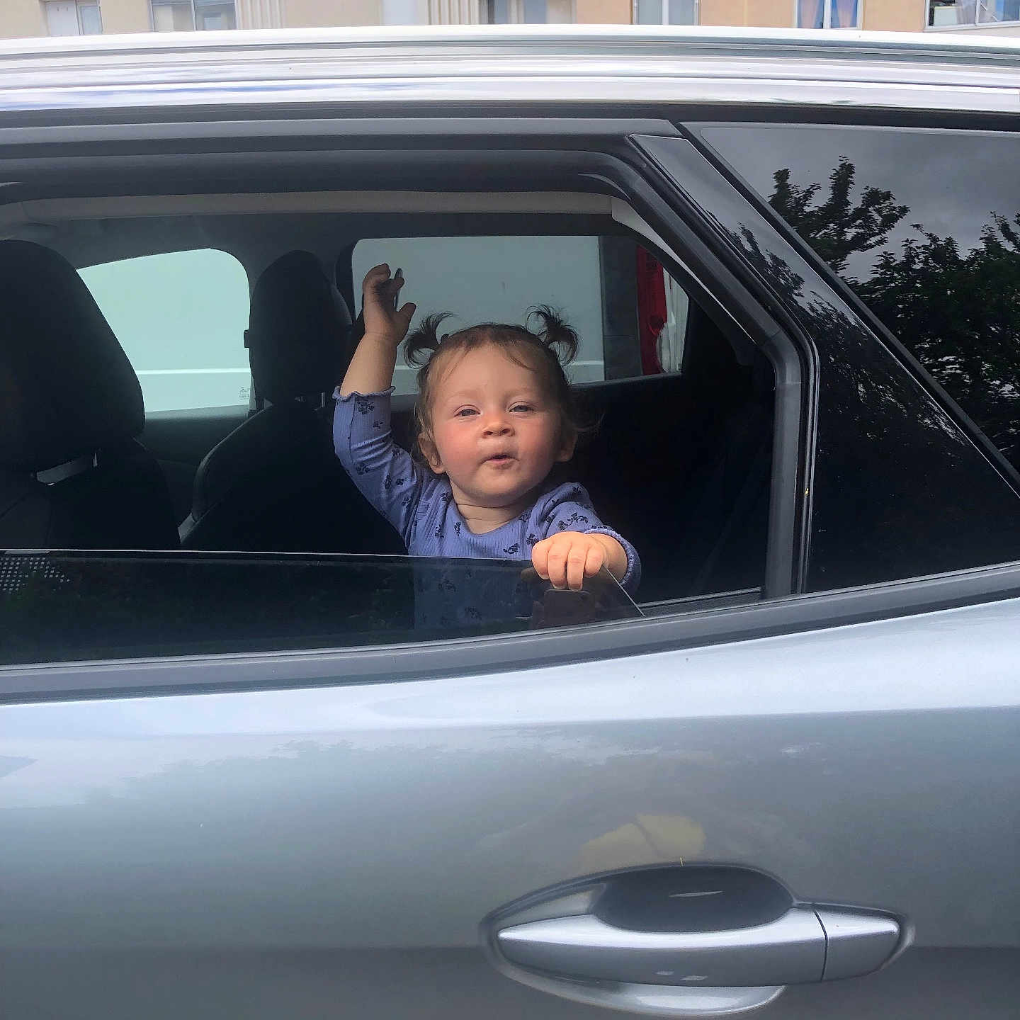 Cataleya a rejoint le concours — aidez-le/la à gagner de superbes lots ! apartment_building, car, car_window, casual_clothing, child, daylight, expression, face, hand, pigtails, portrait, reflection, seat, silver_car, toddler, urban, vehicle, waving, window, young_child