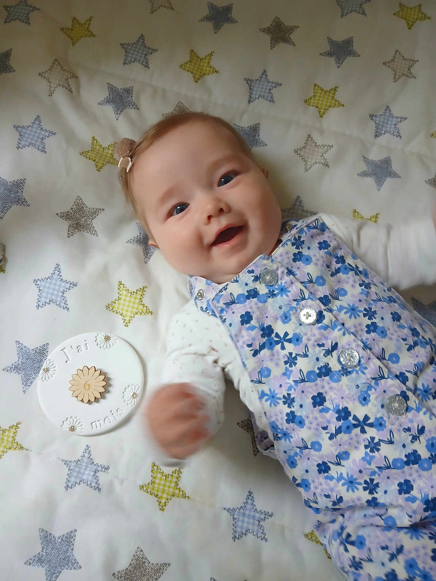 Roxane participe au concours pour gagner de l'argent avec cette photo : baby, infant, smiling, face, hand, blanket, stars, pattern, blue, white, floral, clothing, buttons, plaque, milestone, lying_down, happy, cute, young_child, portrait