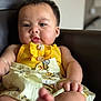 Delilah is registered to the contest to win money with this photo: baby, child, infant, yellow_dress, bee_pattern, armchair, indoor, portrait, face, hand, foot, skin, cute, chubby, clothing, furniture, relaxing, seated, person, soft_light