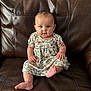 baby, child, infant, floral_dress, leather_couch, sitting, indoors, curious, foot, barefoot, chubby_cheeks, portrait, furniture, person, young_child, looking_at_camera, cute, casual, home_interior, relaxed