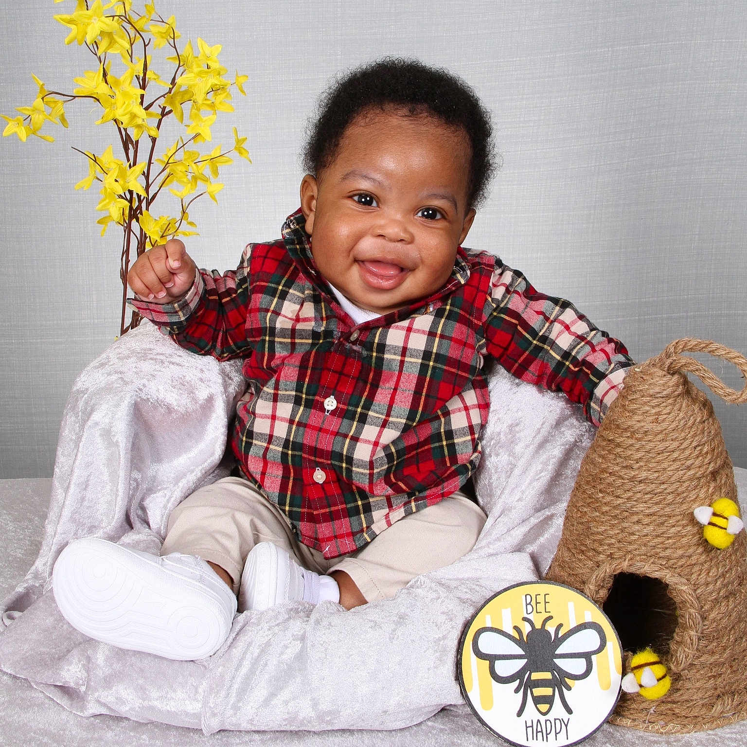 Gyaire is registered to the contest to win money with this photo: baby, child, smile, plaid_shirt, beige_pants, white_shoes, yellow_flowers, bee, beehive, decor, soft_blanket, chair, indoor, cute, happy, portrait, person, sitting, cozy, background
