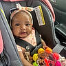baby, child, car_seat, toy, headband, seatbelt, infant, cute, smiling, colorful, floral, clothing, car_interior, safety, young_child, portrait, happy, person, indoors, baby_girl