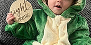 Nora joined the competition — help win amazing prizes! baby, infant, child, frog_costume, green_costume, hood, milestone_sign, wooden_disc, eight_months, sofa, textured_sofa, plush, portrait, sitting, hand, eyes, mouth_open, cute, home_interior, photography