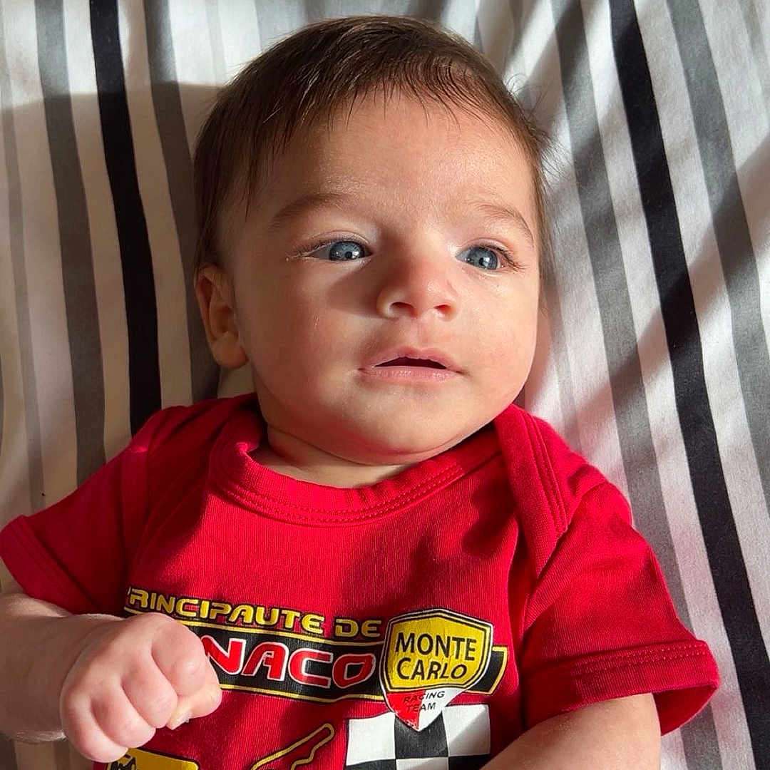 Nidal participe au concours pour gagner de l'argent avec cette photo : baby, blue_eyes, casual, close_up, clothing, cute, expression, fist, indoor, infant, lying_down, monte_carlo, person, portrait, racing_shirt, red_shirt, small_hands, soft_lighting, striped_blanket, young_child