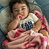 baby, infant, child, portrait, smiling, happy, sitting, blanket, pink_blanket, baby_seat, blue_chair, indoors, face, dark_hair, brown_eyes, hand, finger_sucking, white_shirt, clothing, cozy