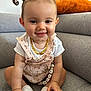Inaya participe au concours pour gagner de l'argent avec cette photo : baby, child, smiling, pigtails, romper, socks, couch, indoor, happy, face, person, seated, cute, playful, infant, jewelry, necklace, skin, hand, footwear