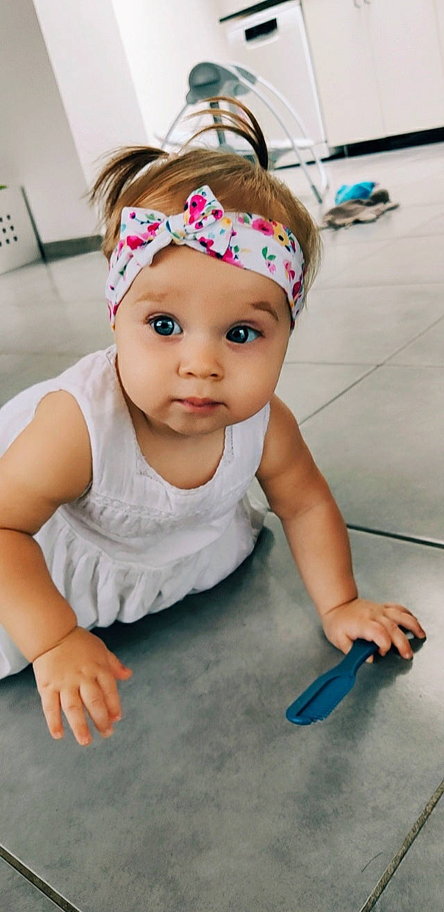 Inaïa a rejoint le concours — aidez-le/la à gagner de superbes lots ! baby, baby_toddler_clothing, cap, cheek, child, clothing, dress, eye, finger, floor, flooring, fun, happy, headgear, headwear, kitchen_utensil, person, skin, sleeve, smile