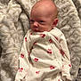 baby, newborn, infant, onesie, cherry_print, blanket, towel, potty, face, portrait, indoor, carpet, pajamas, cute, expression, gaze, bald_head, skin, floor_tile, soft_texture