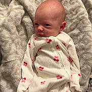 Hazel is registered to the contest to win money with this photo: baby, newborn, infant, onesie, cherry_print, blanket, towel, potty, face, portrait, indoor, carpet, pajamas, cute, expression, gaze, bald_head, skin, floor_tile, soft_texture