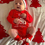 Alex participe au concours pour gagner de l'argent avec cette photo : baby, infant, christmas, red_clothing, santa_hat, socks, blanket, festive, holiday, cute, face, hands, legs, decoration, christmas_tree, indoors, portrait, smiling, soft_light, laying_down
