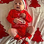 baby, infant, christmas, red_clothing, santa_hat, socks, blanket, festive, holiday, cute, face, hands, legs, decoration, christmas_tree, indoors, portrait, smiling, soft_light, laying_down
