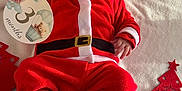 Alex participe au concours pour gagner de l'argent avec cette photo : baby, infant, santa_costume, red_clothing, christmas_theme, holiday, milestone_card, soft_blanket, festive, cute, indoors, footwear, red_hat, face, person, lying_down, holiday_decorations, christmas_trees, smiling, celebration