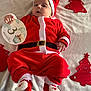 baby, infant, santa_costume, red_clothing, christmas_theme, holiday, milestone_card, soft_blanket, festive, cute, indoors, footwear, red_hat, face, person, lying_down, holiday_decorations, christmas_trees, smiling, celebration