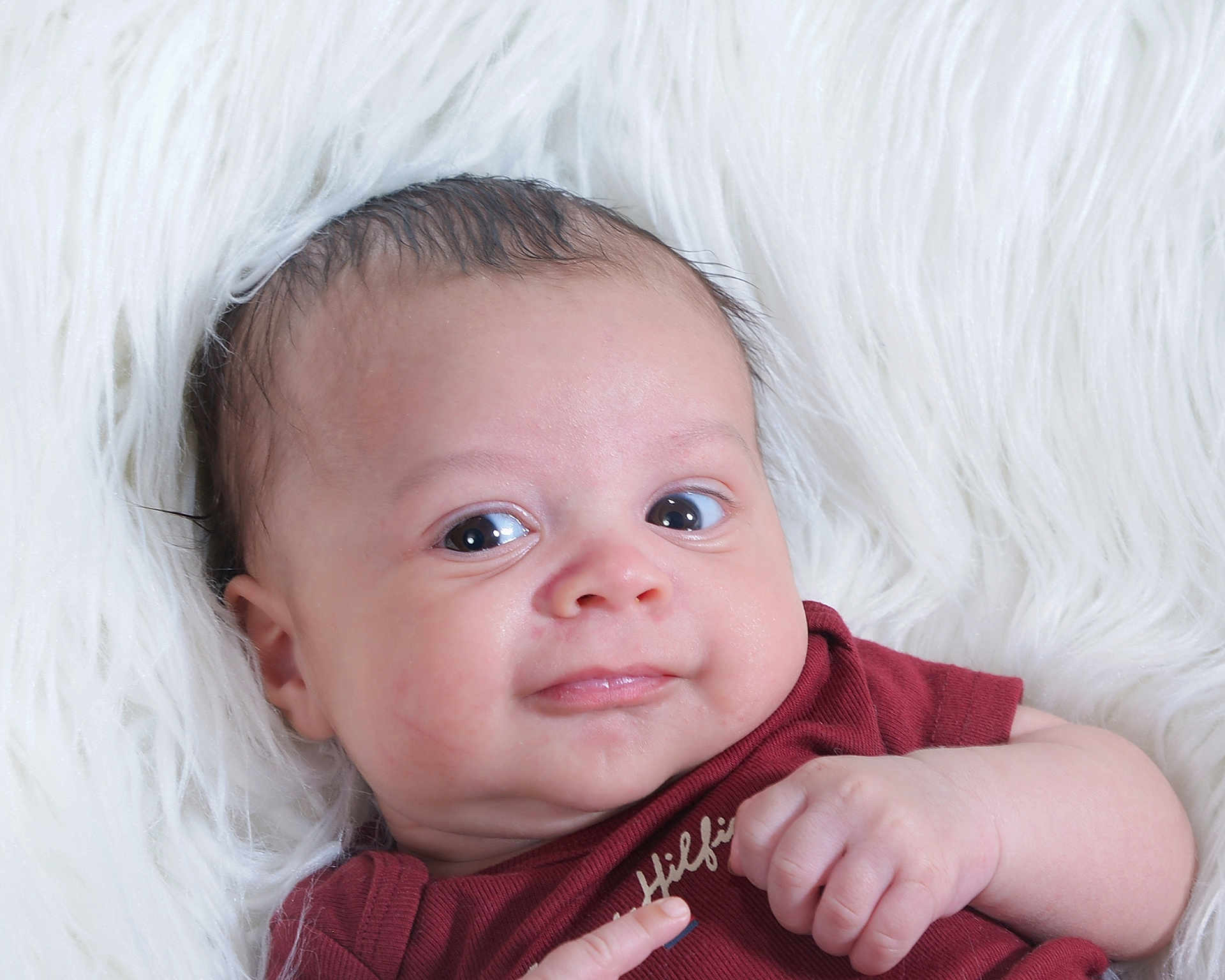 Jasiah is registered to the contest to win money with this photo: baby, infant, smile, face, eyes, hand, skin, hair, clothing, maroon, white_background, fluffy, portrait, cute, child, newborn, expression, lying_down, soft_texture, closeup