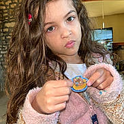Emma a rejoint le concours — aidez-le/la à gagner de superbes lots ! background, badge, casual, child, closeup, clothing, curly_hair, expression, face, fuzzy, girl, holding, indoor, long_hair, person, pink_jacket, portrait, stone_wall, television, young