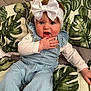 Marliya-Mae is registered to the contest to win money with this photo: baby, child, infant, headband, bow, denim_overalls, hand, blue_eyes, couch, pillow, leaf_pattern, fabric, sitting, cute, playful, indoor, portrait, smiling, clothing, person